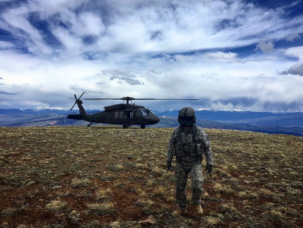 A hoist operator standing before a landed Black Hawk on an Alaska mountain ridge